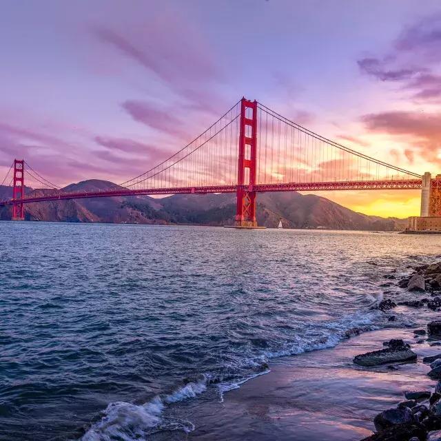El puente Golden Gate al atardecer con un cielo multicolor y la Bahía de San Francisco en primer plano.