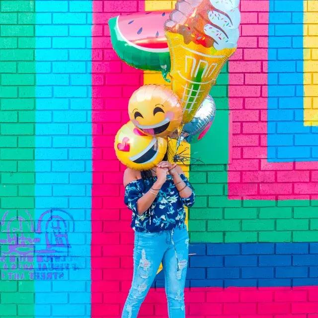 Uma menina comemora seu aniversário com balões em frente a um mural colorido.
